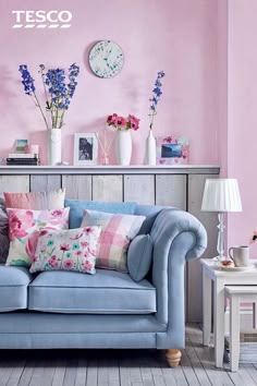 This may contain: a blue couch sitting next to a table with flowers in vases on top of it